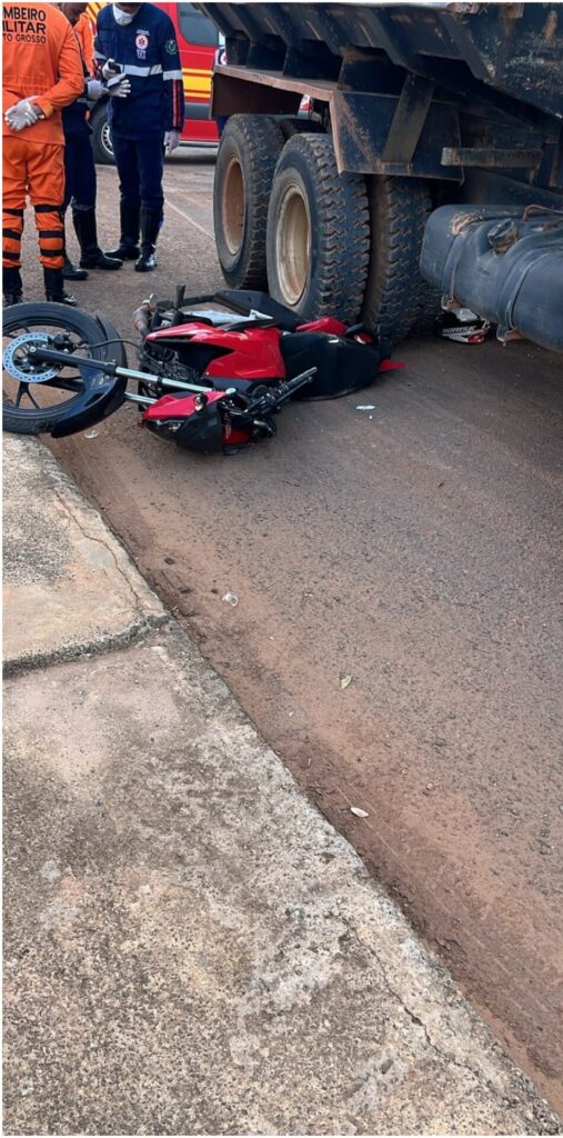 Moto vermelha caída ao lado das rodas de um caminhão, com bombeiros e equipe do Samu ao fundo, no Jardim das Palmeiras