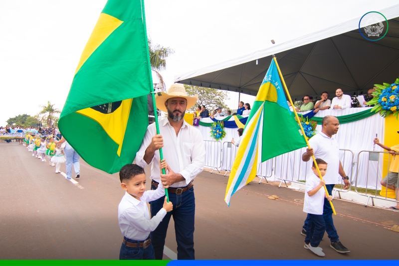 Homem e criança conduzem as bandeiras do Brasil e de Sapezal durante o Desfile Cívico, MT