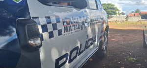 Lateral de viatura branca e azul da Polícia Militar de Mato Grosso estacionada em pátio de terra