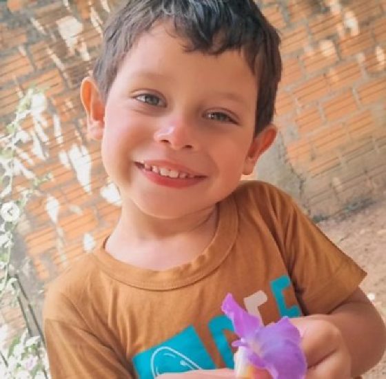Henry Gabriel Santos, menino de 4 anos, sorri segurando uma flor