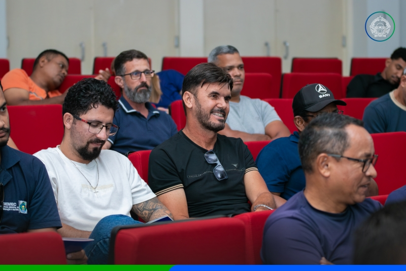 Homens sentados em poltronas vermelhas de auditório acompanham palestra sobre segurança no trânsito em Sapezal