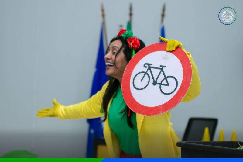Atriz com figurino amarelo e verde segura placa de trânsito de proibido bicicleta durante apresentação em Sapezal