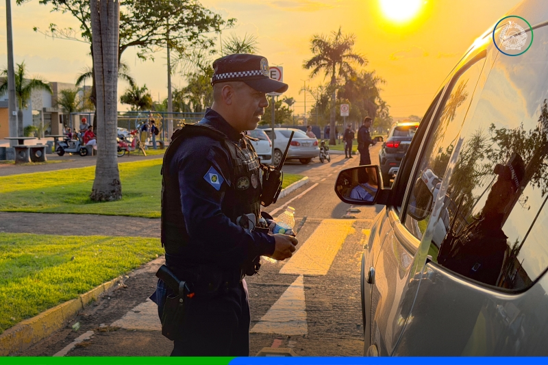 Agente de trânsito uniformizado conversa com motorista ao lado de carro prata em avenida de Sapezal, ao pôr do sol