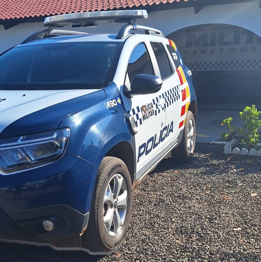 Viatura da Polícia Militar de Mato Grosso, caminhonete azul e branca com giroflex, estacionada em frente à unidade da PM
