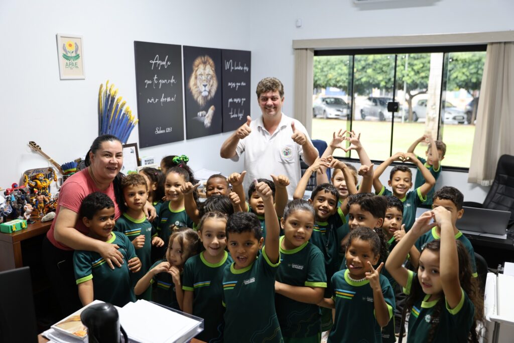 Alunos de uniforme verde da rede municipal posam sorridentes com professora e vereador em gabinete da Câmara de Campo Novo do Parecis