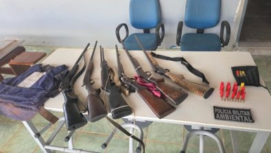 Espingardas, revólver, munições e colete balístico apreendidos pela Polícia Militar Ambiental sobre uma mesa