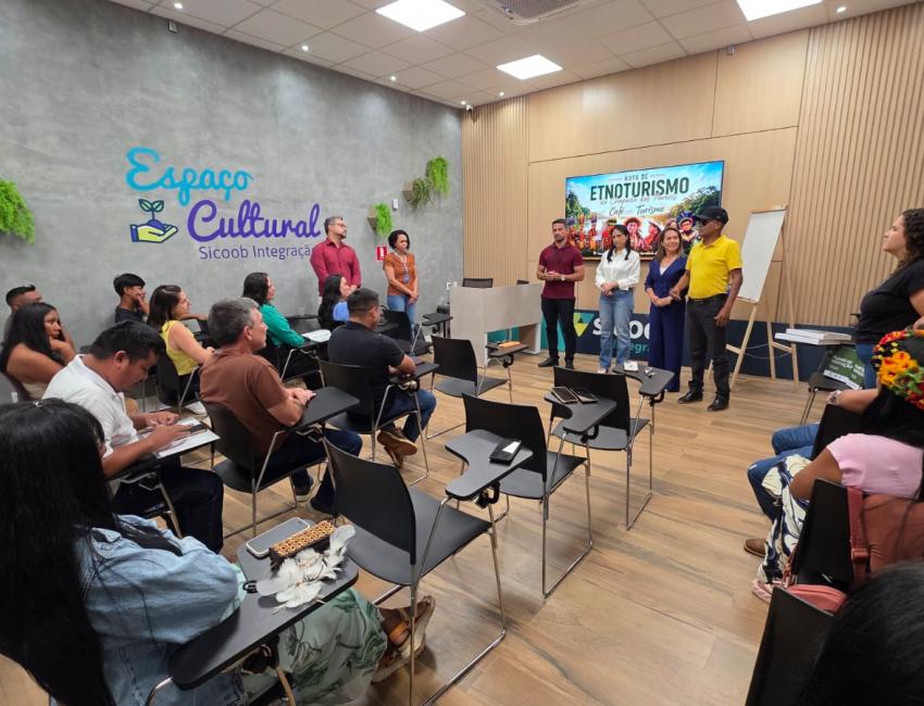 Participantes sentados em auditório assistem à apresentação da Rota de Etnoturismo Chapada dos Parecis, com telão ao fundo, em Brasnorte