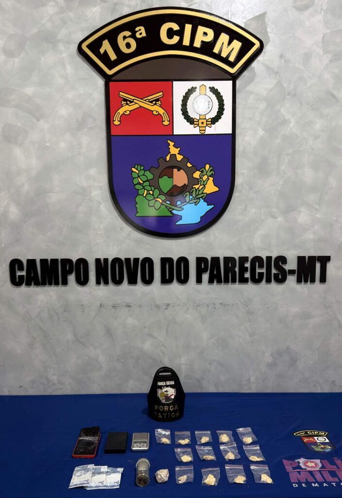 Porções de pasta base de cocaína, balanças de precisão, celular com tela quebrada e notas de dinheiro sobre mesa azul, abaixo do brasão da 16ª CIPM