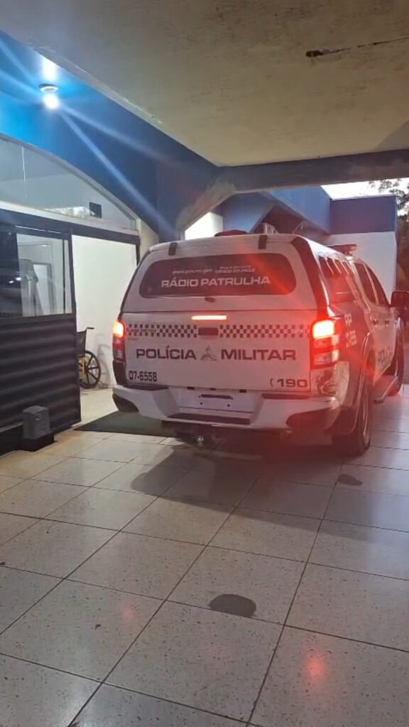Viatura da Polícia Militar estacionada sob uma cobertura, à noite, com as luzes traseiras acesas