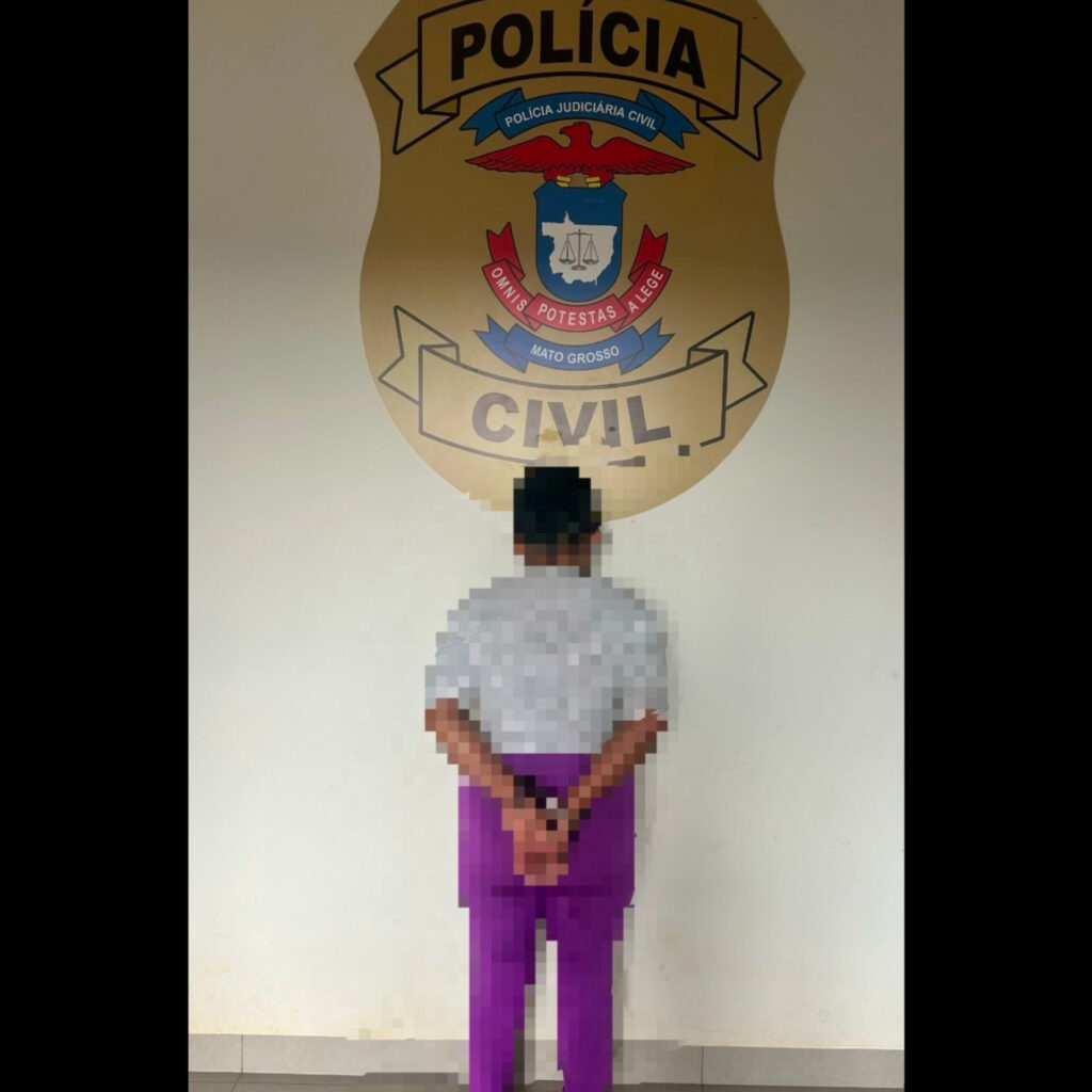 Mulher de costas, algemada e com a imagem desfocada, em frente ao brasão da Polícia Judiciária Civil de Mato Grosso