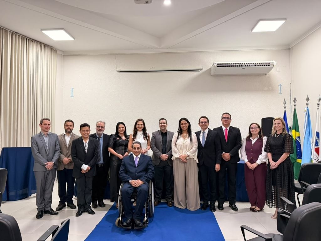 Grupo de advogados e dirigentes da OAB posa em auditório, com um homem em cadeira de rodas à frente e bandeiras ao fundo