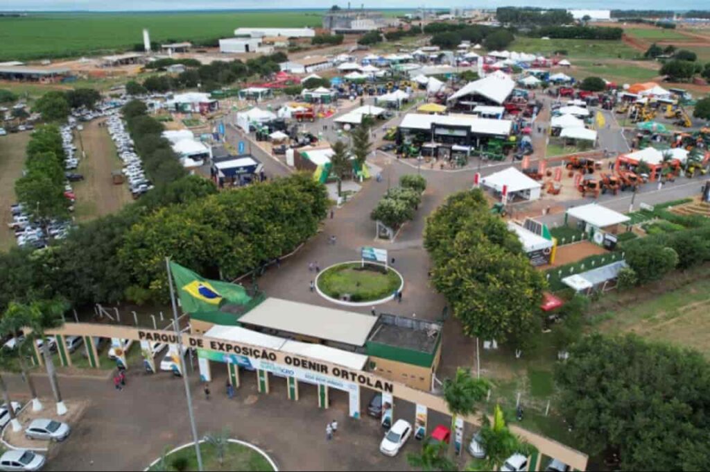 Vista aérea do Parque de Exposição Odenir Ortolan com estandes, máquinas agrícolas e carros estacionados durante a feira