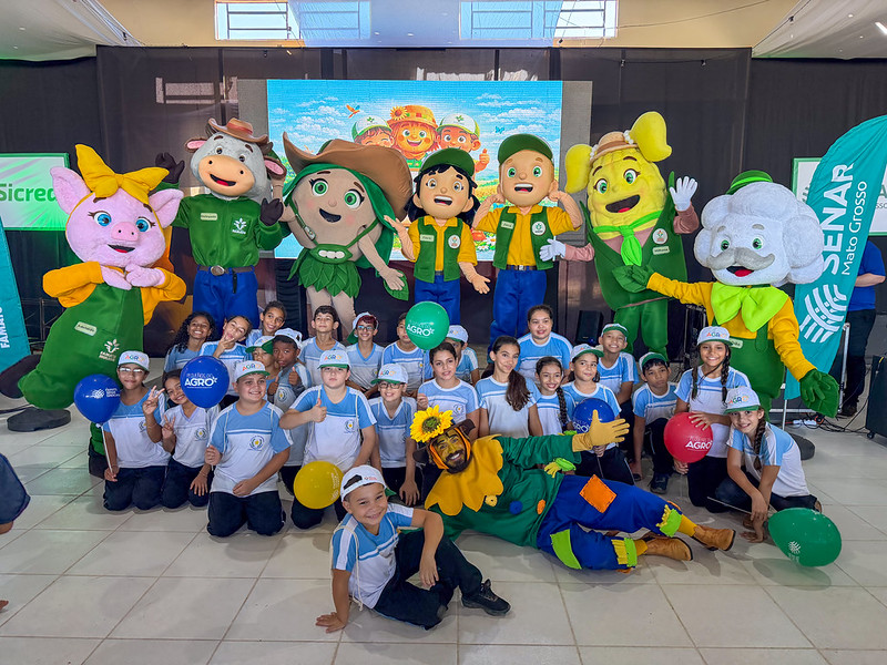 Crianças de uniforme escolar posam com bonecos e mascotes do Programa Pequenos do Agro, como porco, vaca e milho, durante evento do Sistema Famato
