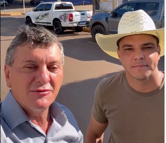 Prefeito Edilson Piaia, de camisa social azul-clara, e o vereador Djonathan Baioto, de chapéu de cowboy branco, em selfie numa rua com caminhonetes ao fundo