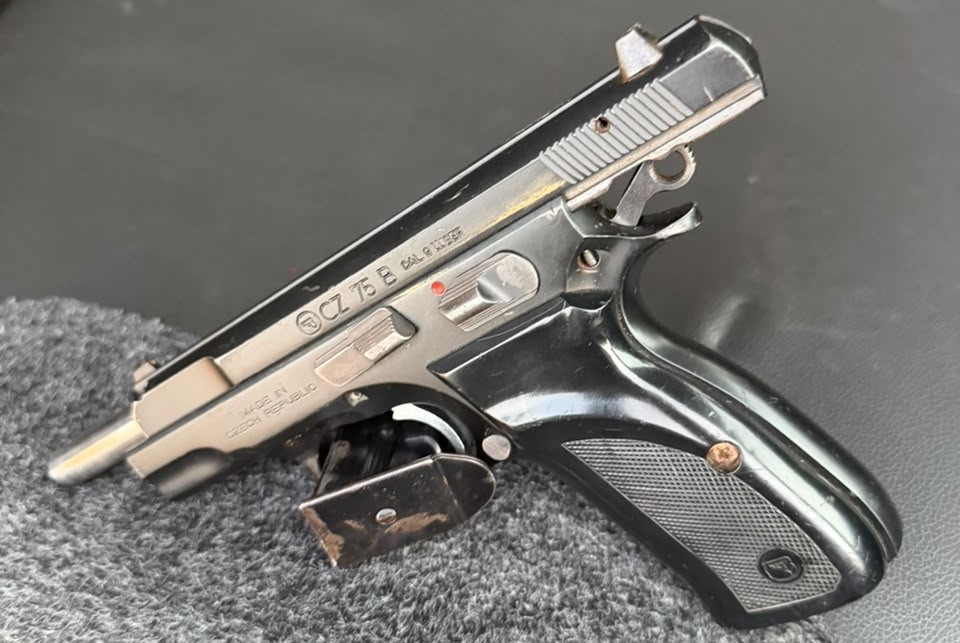 Pistola calibre 9 mm preta e prateada, com carregador, sobre um tecido cinza