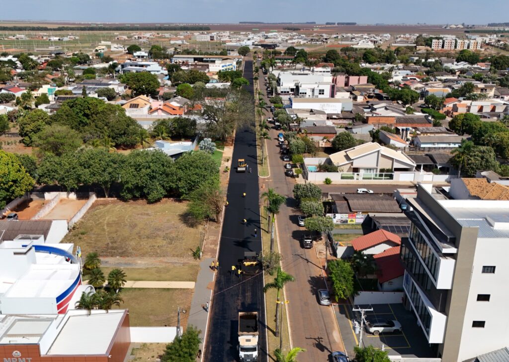 Vista aérea de avenida de Campo Novo do Parecis recebendo nova camada de asfalto, com caminhão, rolo compactador e trabalhadores